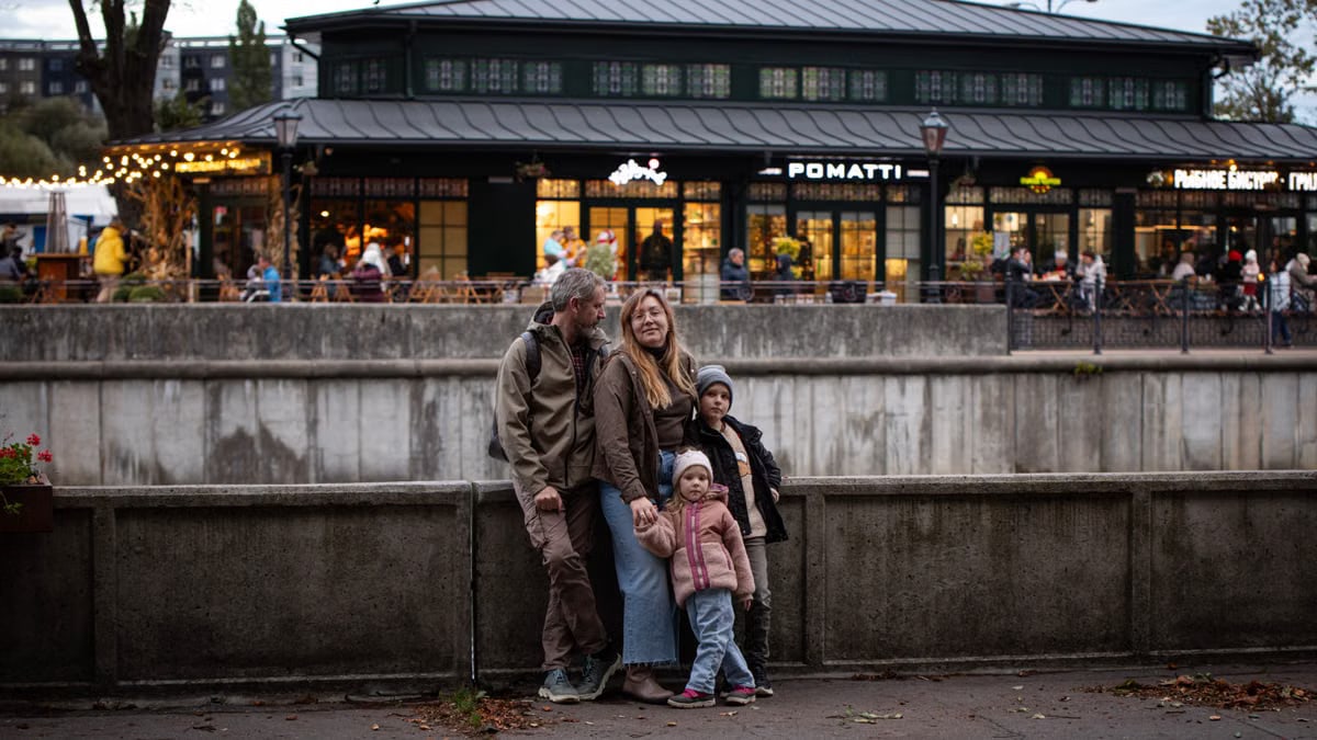 Family of four smiling outdoors in front of a lit café, creating a warm atmosphere in the evening.
